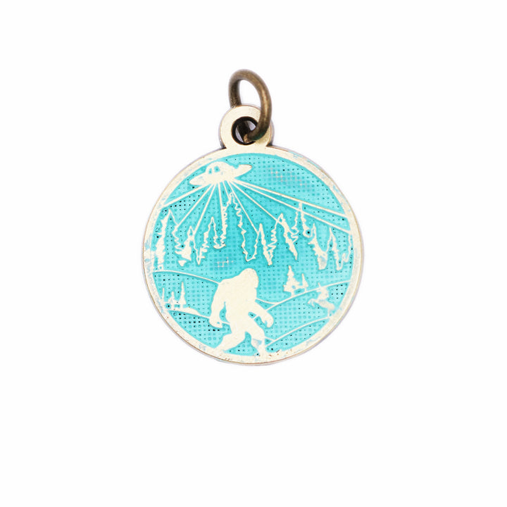 Whimsical charm with illustration of bigfoot, a UFO and a unicorn. The reverse says "Believe in Yourself." Antique bronze painted turquoise and burnished.
