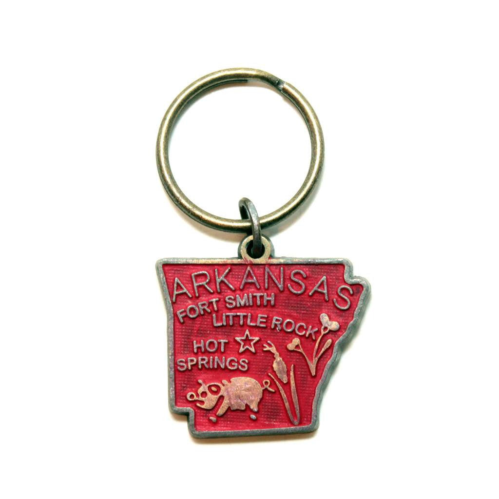 Antique bronze 1 5/8" charm keychain on 1 1/4" keyring. Hand-painted red. Map depicts location of Fort Smith, Little Rock and Hot Springs. It has agricultural illustrations like a pig and corn.