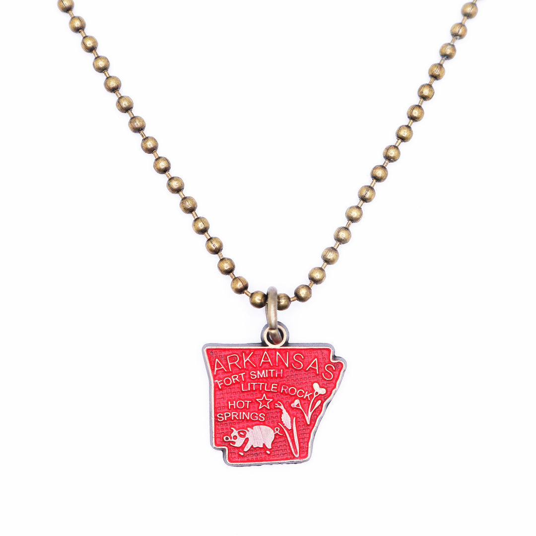 Antique bronze Arkansas state map charm painted red and burnished to shiny gold. Map depicts location of Fort Smith, Little Rock and Hot Springs. It has agricultural illustrations like a pig and corn. Shown on an 18" antique bronze ball chain.