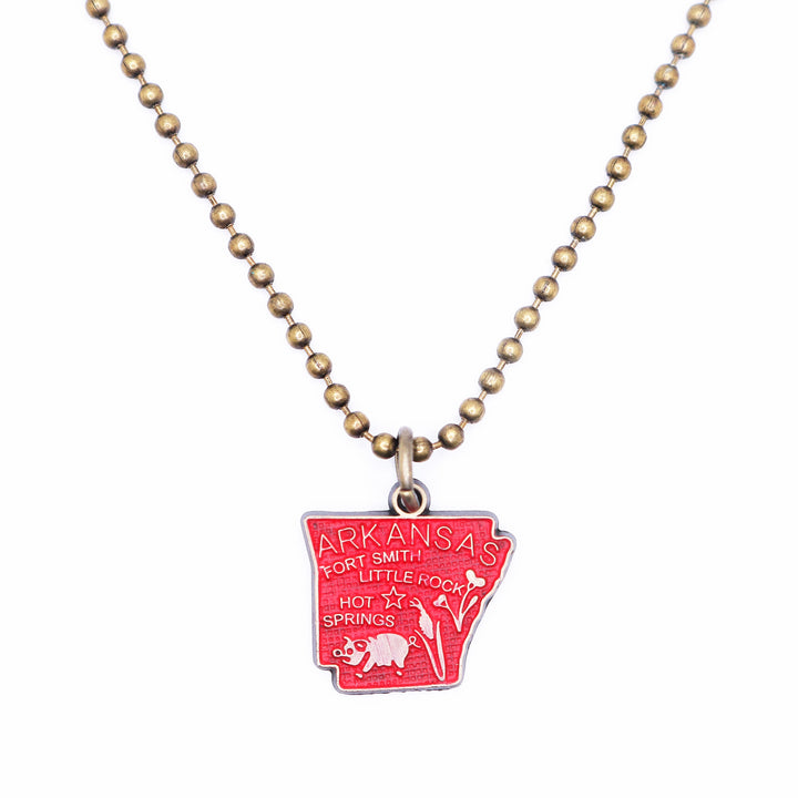 Antique bronze Arkansas state map charm painted red and burnished to shiny gold. Map depicts location of Fort Smith, Little Rock and Hot Springs. It has agricultural illustrations like a pig and corn. Shown on an 18" antique bronze ball chain.