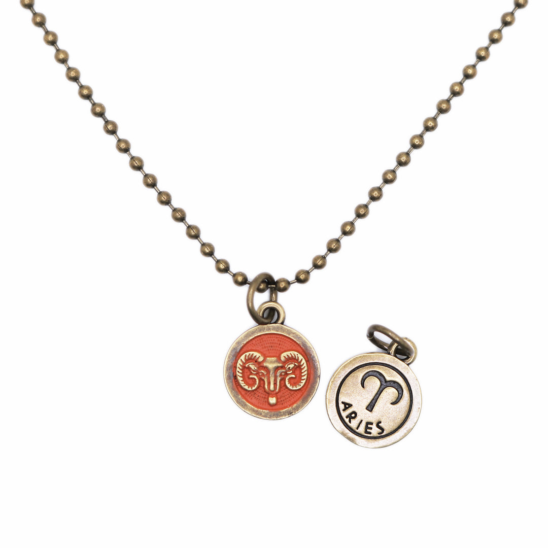 Brass-tone Aries zodiac charm painted orange. One side is illustrated with a ram. Reverse side shows the ram side and says "ARIES".