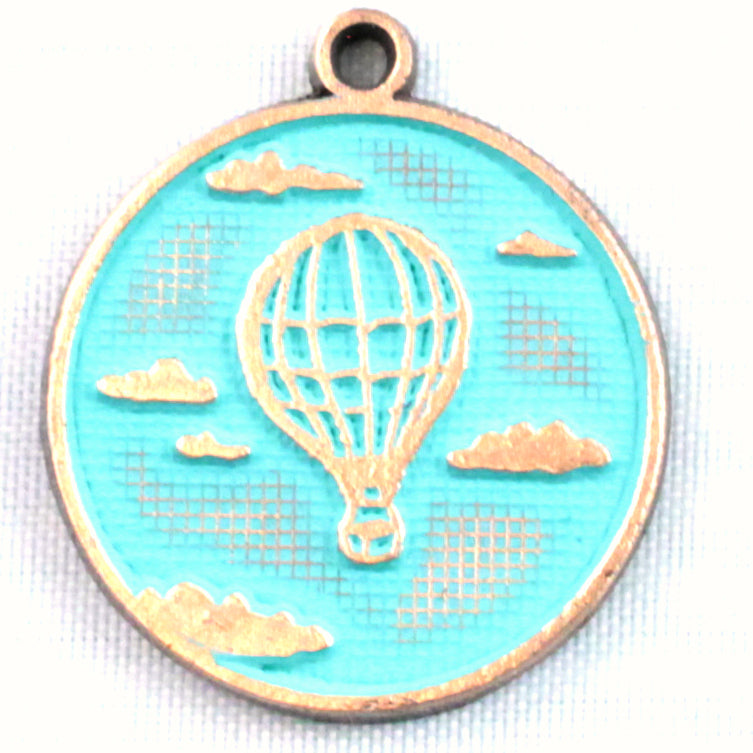 Antique bronze charm painted turquoise and burnished to shiny gold. One side depicts a hot air balloon floating in the clouds. Reverse side says "Adventure Awaits".