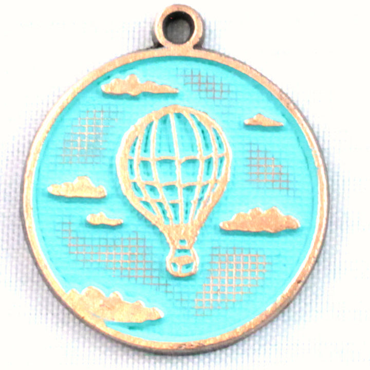 Antique bronze charm painted turquoise and burnished to shiny gold. One side depicts a hot air balloon floating in the clouds. Reverse side says "Adventure Awaits".