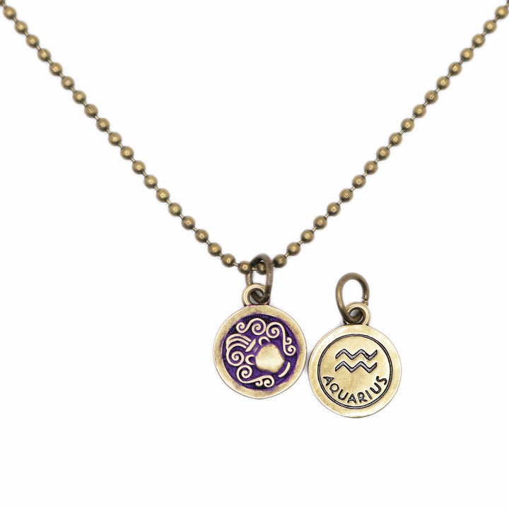 Brass-tone Aquarius zodiac charm painted purple. One side depicts an urn overflowing with water. Reverse side shows the water sign and says "AQUARIUS". Shown on an 18" antique bronze ball chain.