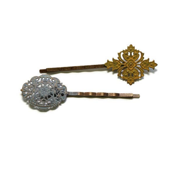 Mismatched filigree charms on bobby pins. Hand-painted light gray and mustard yellow. Intricate Victorian flourishes for vintage bobby pin appeal.