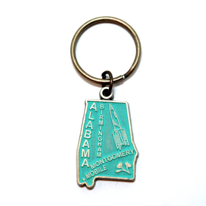 Antique bronze 1 1/4" charm keychain on 1 1/4" keyring. Alabama state charm painted turquoise and burnished to shiny gold. Map depicts location of Birmingham, Montgomery and Mobile and shows a rocket ship.