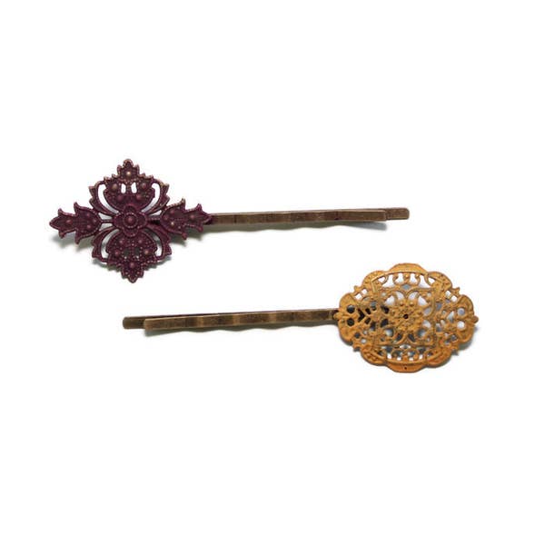 Mismatched filigree charms on bobby pins. Hand-painted mauve and ginger yellow. Intricate Victorian flourishes for vintage bobby pin appeal.