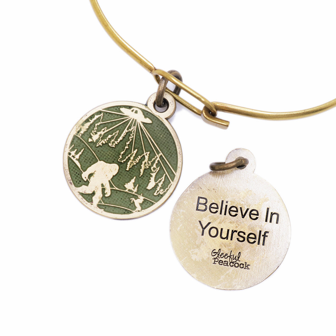 Whimsical charm with illustration of bigfoot, a UFO and a unicorn. The reverse says "Believe in Yourself." Antique bronze painted olive green and burnished.