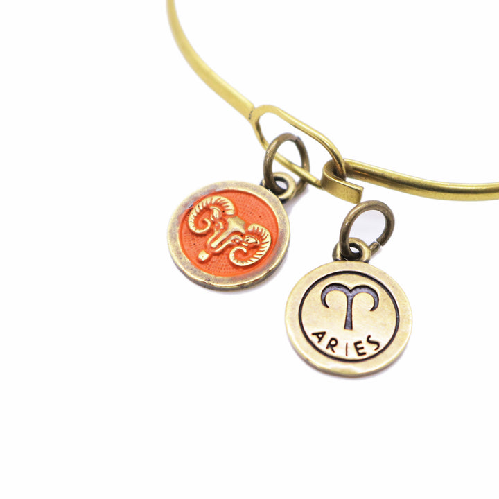 Brass-tone Aries zodiac charm painted orange. One side is illustrated with a ram. Reverse side shows the ram side and says "ARIES".